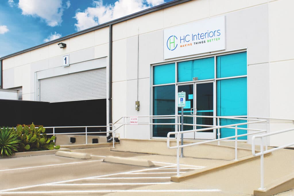 Warehouse building with a large number "1" sign and "HC Interiors" signage, featuring blue-tinted windows and accessible parking spaces.