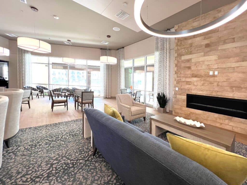 A modern lounge with cozy seating, large windows, and decorative lighting. Features wooden accents, indoor plants, and ample chairs for gathering.