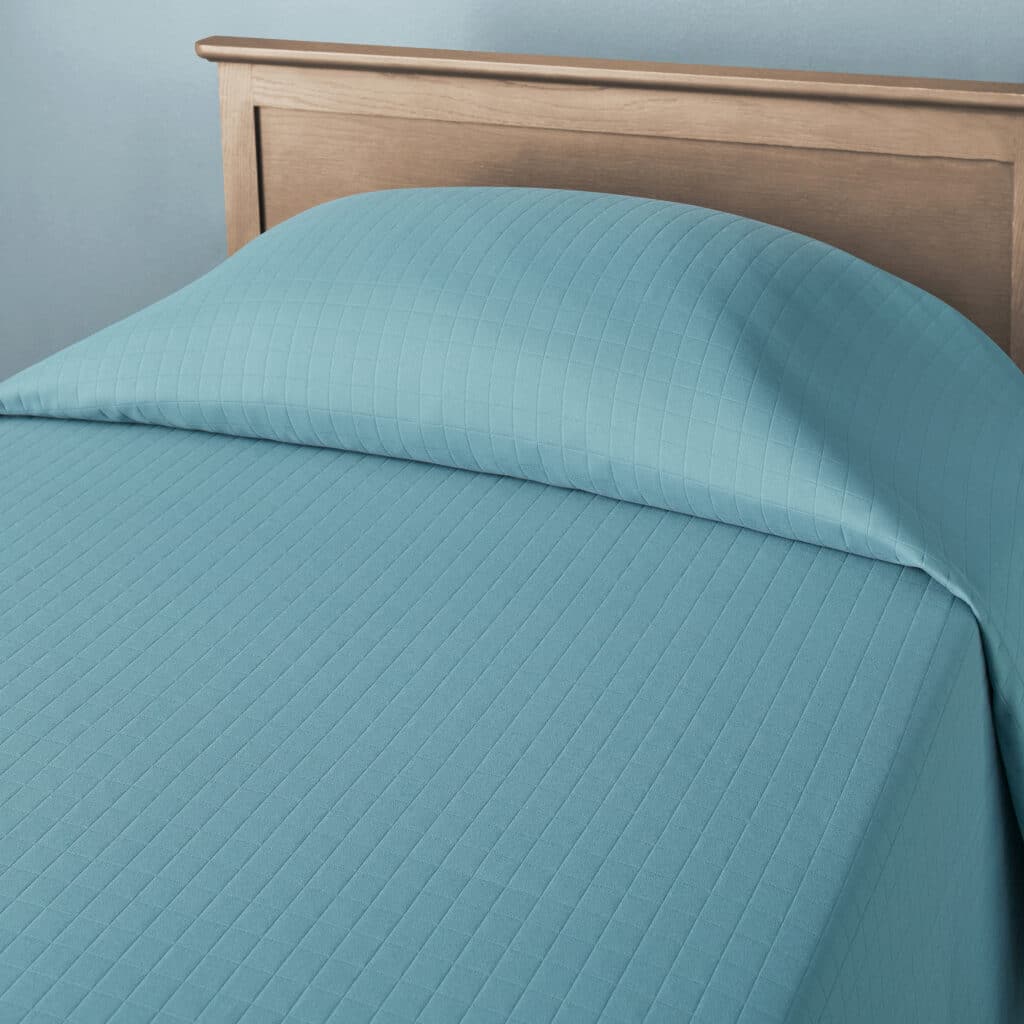 A neatly made bed features a light blue sheet and pillow, against a wooden headboard and soft blue wall, creating a calming atmosphere.