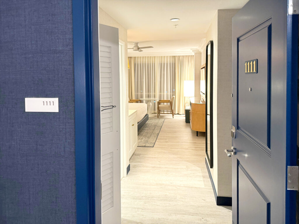 Hotel room 1111 with open door reveals a modern interior, including a bed, floor lamp, chair, and large window with curtains.