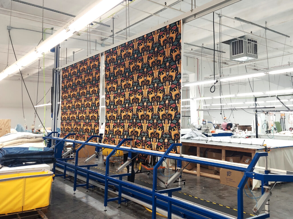 A factory with machinery, colorful patterned fabric rolls, and a person working at a table in a well-lit, industrial space.