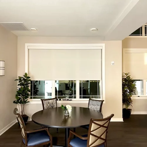 A modern dining area with a round table and four chairs, surrounded by plants. Soft lighting and neutral tones enhance the peaceful atmosphere.