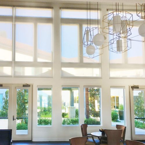 Spacious interior with large windows, geometric light fixtures, and modern seating. Bright natural light illuminates the room, offering views of the garden outside.