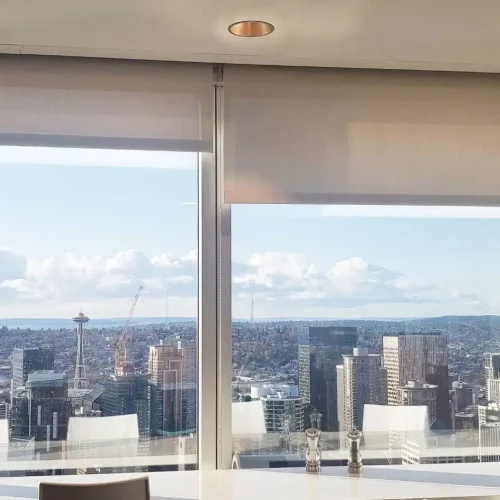 Office interior with a view of Seattle skyline through large windows, featuring the Space Needle. White chairs and flowers adorn the room.