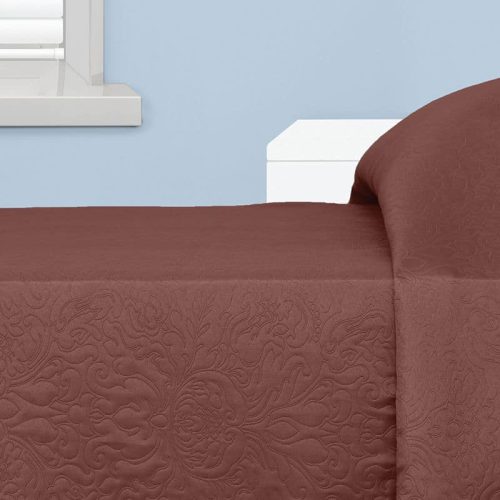 A quilted brown bedspread on a bed, set against a light blue wall near a window with white shutters in a simple room.