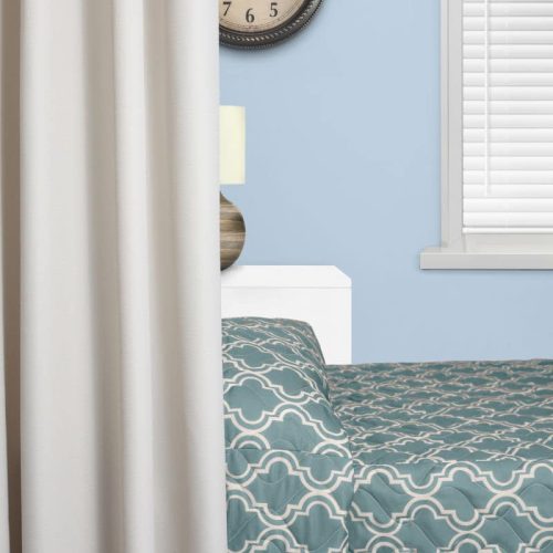 Bedroom corner features a patterned teal bedspread, a wall clock, a lamp, and partially visible window blinds, against a light blue wall.