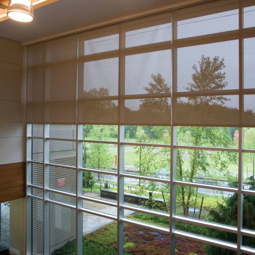 Large indoor window with roller blinds, overlooking a lush green garden. Stylish pendant lights hang above, casting a warm glow inside.