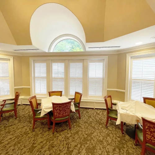 A neatly arranged dining room with wooden chairs and tables, window shutters, and an arched ceiling. No people are present.